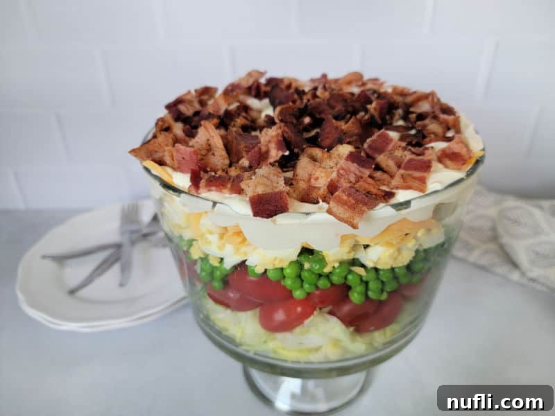 Classic 7 layer salad in a trifle dish with small plates and forks behind it. 
