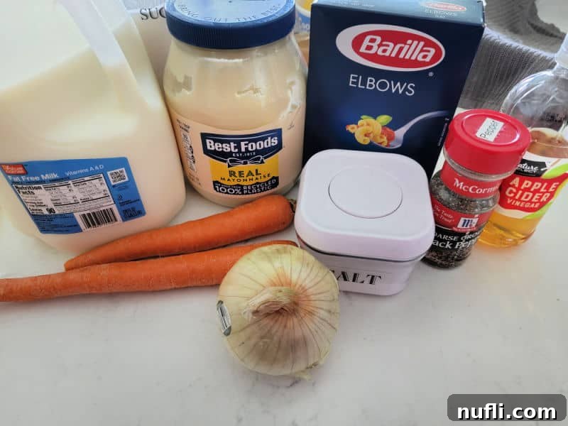 Milk, Best Foods Mayo, Elbow Macaroni, Carrots, Onion, Salt, Black Pepper, and Apple Cider Vinegar on a white counter. 