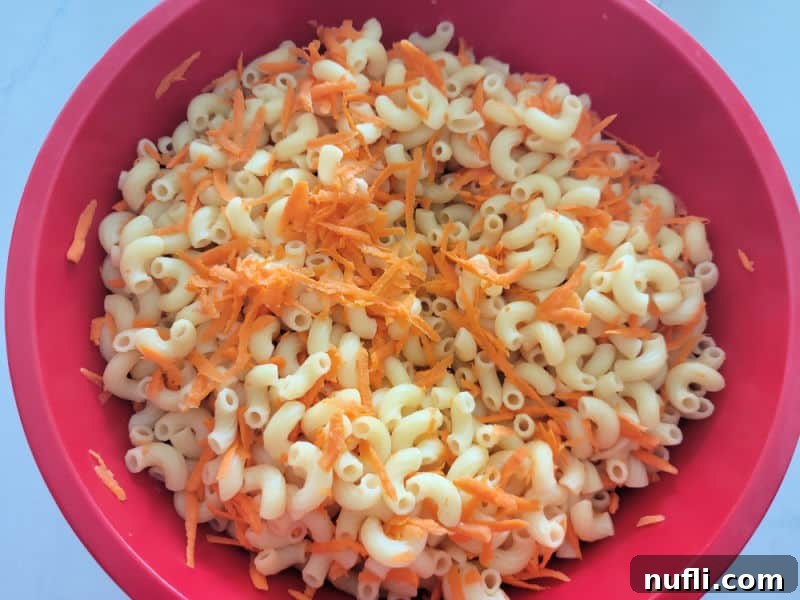 Cooked macaroni pasta and shredded carrots in a large red bowl