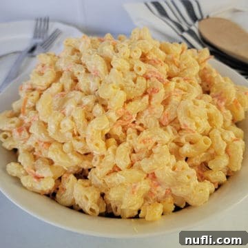 Hawaiian Mac Salad in a white bowl next to plates and a wooden spoon