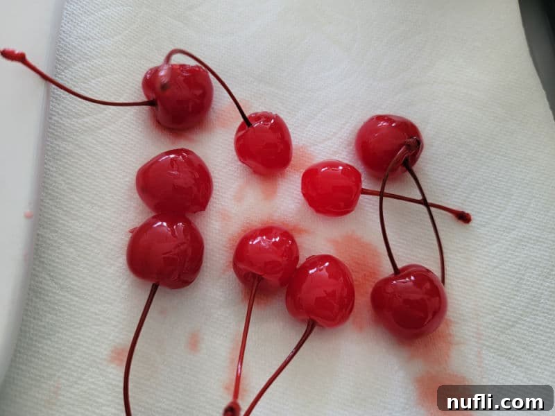 A close-up of bright red maraschino cherries laid out on a paper towel, absorbing excess juice to prevent bleeding.