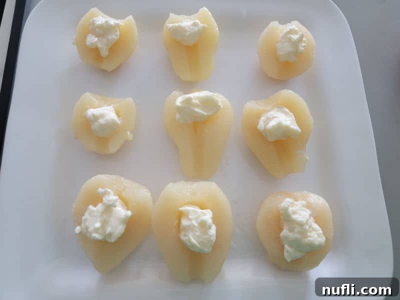 A row of pear halves, each topped with a dollop of creamy mayonnaise, arranged neatly on a pristine white serving platter.