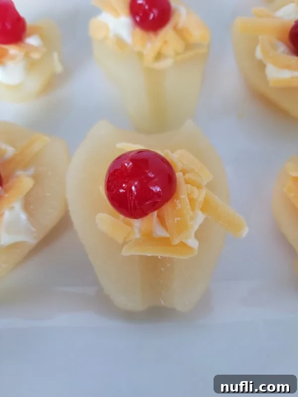 A single maraschino cherry placed perfectly on top of the shredded cheddar cheese and mayonnaise on a pear half, completing the classic look of the Southern Pear Salad.