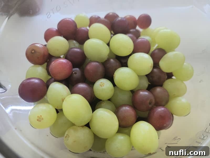 Fresh red and green grapes, sparkling clean and ready for mixing, gathered in a clear glass bowl.