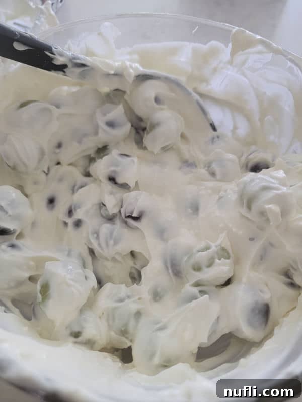 Crisp grapes being gently folded into a luscious, creamy dressing within a large glass bowl, creating a harmonious blend.