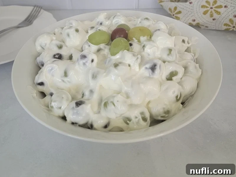 A serving of grape salad in a white bowl, placed on a plate with a fork and a neatly folded cloth napkin beside it.