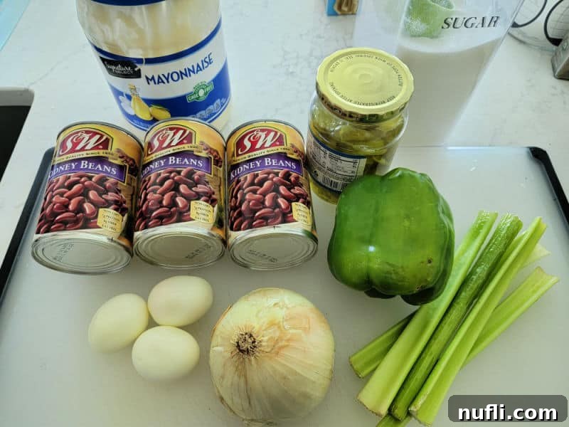 Various kidney bean salad ingredients laid out: mayonnaise, cans of kidney beans, green bell pepper, onion, hard-boiled eggs, sugar, and celery stalks.