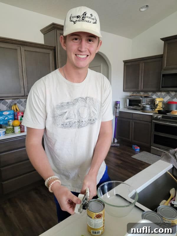 A young man opening a can of kidney beans in a kitchen, preparing them for the salad.
