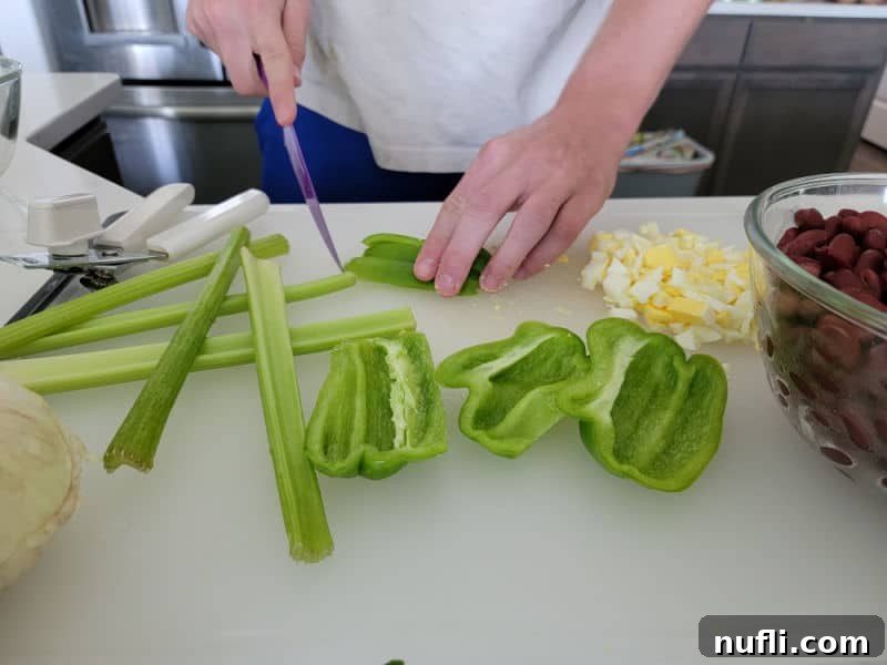 Finely chopped celery stalks and green peppers on a cutting board, alongside hard-boiled eggs, ready for the salad.