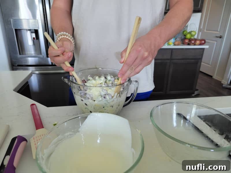 Hands mixing kidney bean salad in a glass bowl with two wooden spoons, ensuring all ingredients are well combined.
