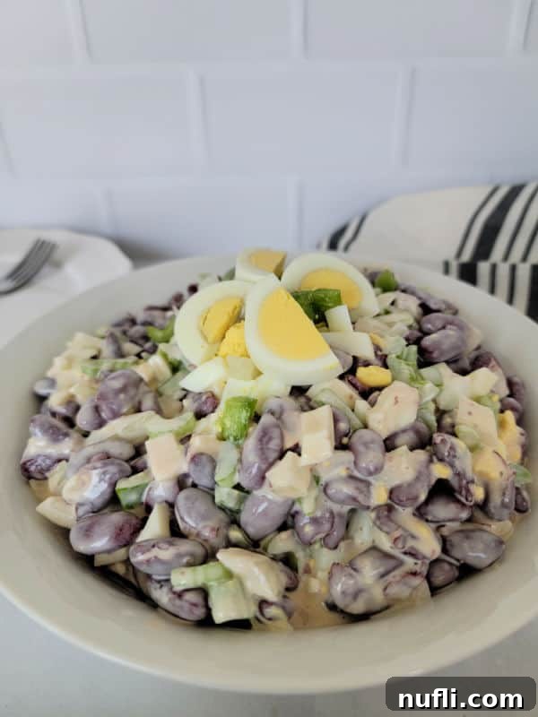 Close-up of hard-boiled eggs cut into slices, elegantly garnishing kidney bean salad in a white bowl next to a cloth napkin.