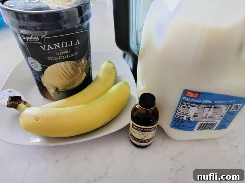 banana milkshake ingredients on a counter with vanilla ice cream, bananas, vanilla, and fat free milk next to a blender