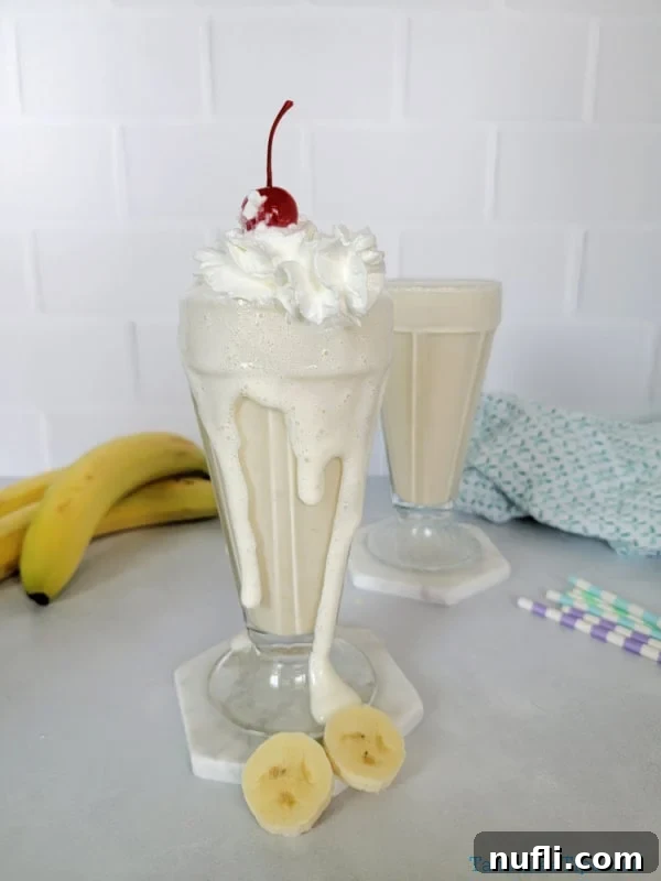 Two banana milkshakes in shake glasses with whipped cream and maraschino cherry garnish