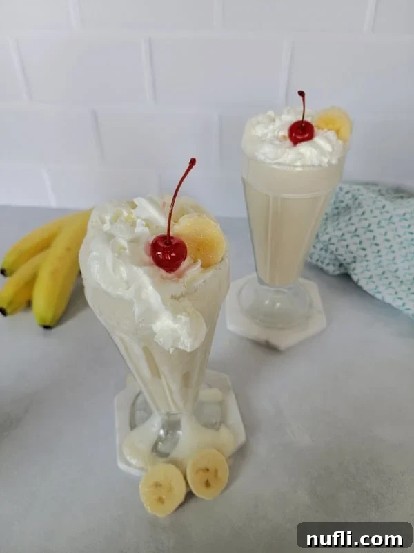 Two banana milkshakes in shake glasses with whipped cream and maraschino cherry garnish
