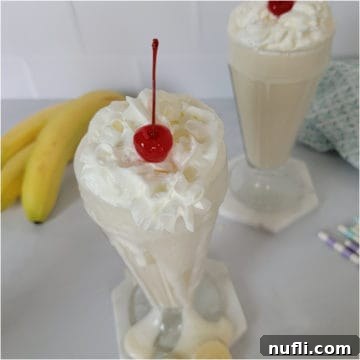 Banana milkshake with whipped cream and a cherry next to bananas and paper straws