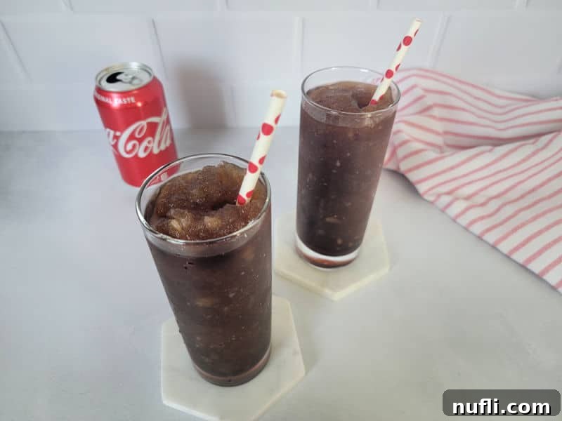 Two Coke slushies in tall glasses next to an open can of Coca Cola and a red striped cloth napkin