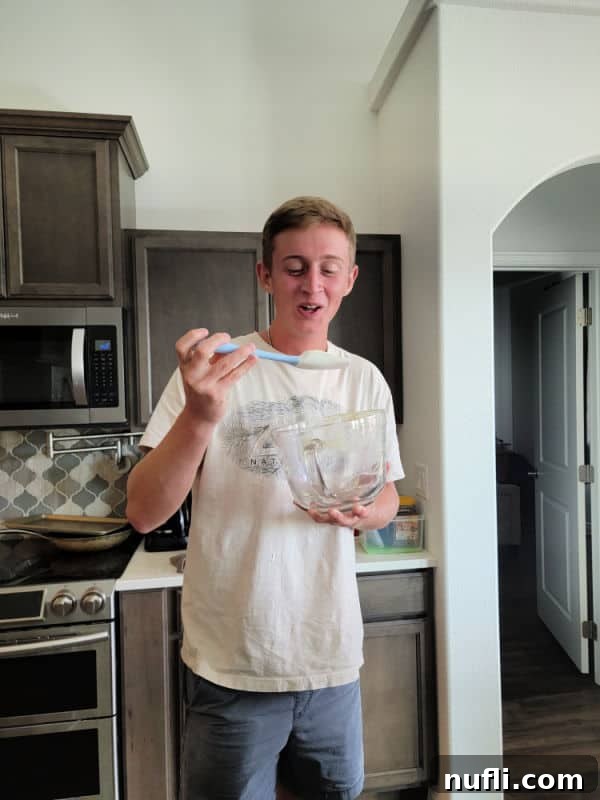 teenage boy with a spatula and glass bowl mixing ingredients for the cake
