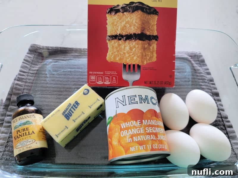 glass baking dish with vanilla, butter, cake mix, mandarin oranges, and eggs in it, ingredients for Pig Pickin Cake
