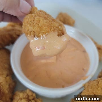 Chicken nugget dipping into Boom Boom sauce in a white bowl