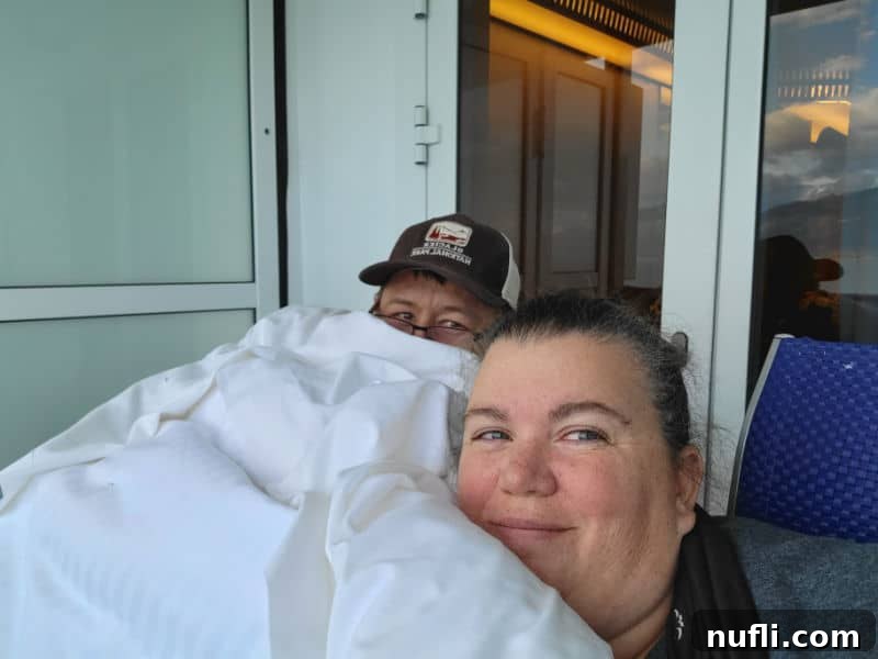 Tammilee and John covered in a white comforter on the balcony of the Carnival Miracle 