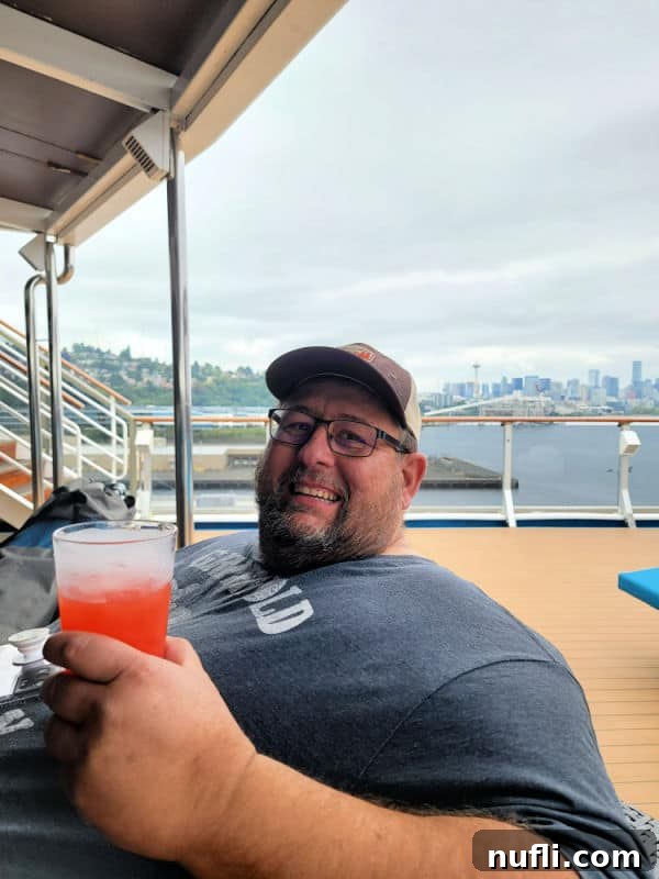 John holding a tropical drink with the skyline of Seattle in the background from the Carnival Miracle Cruise Ship 