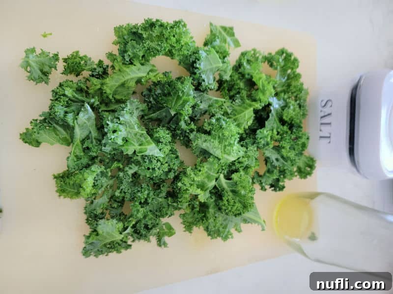 Fresh kale on a cutting board, with olive oil and salt nearby, ready for preparation.