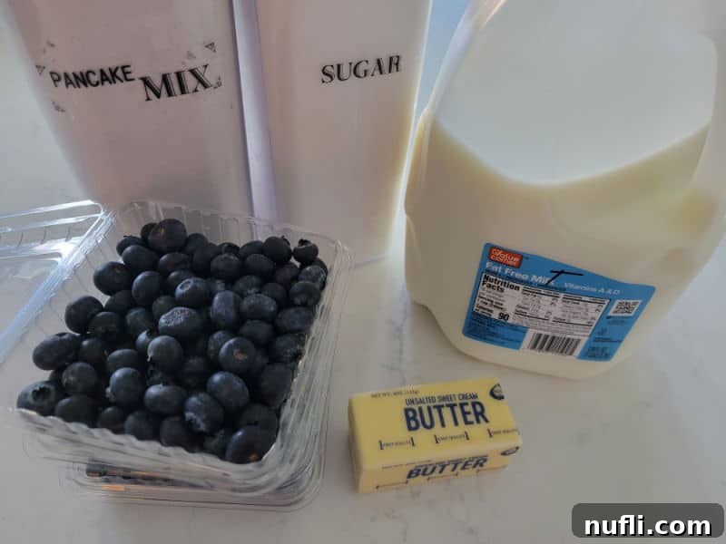 Pancake mix, sugar, fresh blueberries, butter, and milk on a white marble counter
