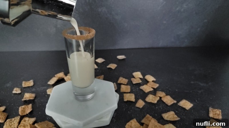 Cocktail shaker pouring into a shot glass on marble coasters with cinnamon toast crunch cereal spread around it