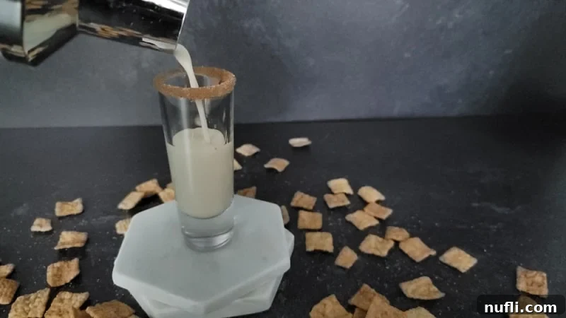 Sweet Cinnamon Crunch Shooter 6 Cocktail shaker pouring into a shot glass on marble coasters with cinnamon toast crunch cereal spread around it