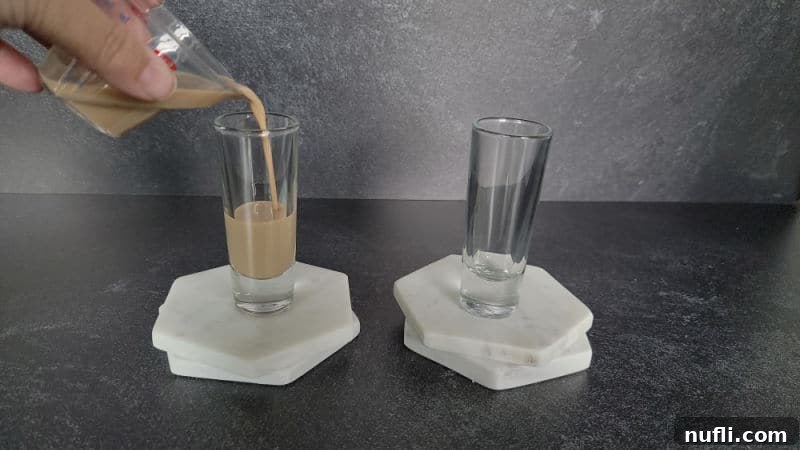 Hand pouring a jigger of Baileys Irish Cream into a shot glass for a Cement Mixer Shot