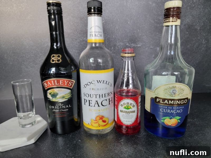 glass shot glass on a marble coaster, bottles of Baileys Irish cream, southern peach schnapps, grenadine, and blue curacao