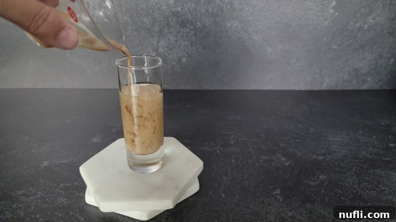 cream liquid pouring into clear liquid in a shot glass on two marble coasters