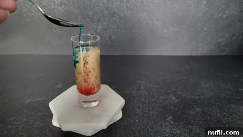 Alien Brain Hemorrhage Shot How To 6 blue liquid pouring off a spoon into cream, red and clear liquid in a shot glass on two coasters.