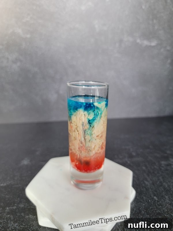 blue liquid floating on cream and red liquid in a shot glass on two coasters