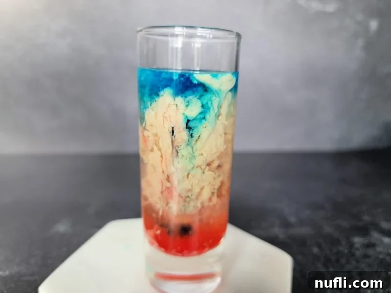 Alien Brain Hemorrhage Shot How To 8 blue, cream, and red liquid swirling in a glass shot glass sitting on a marble coaster