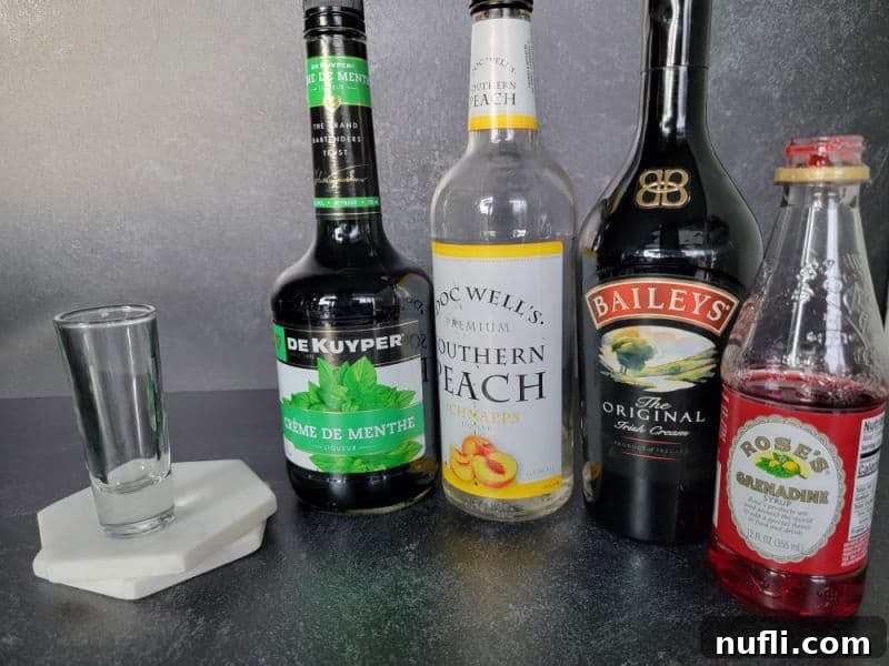 Shot glass next to bottles of creme de menthe, peach schnapps, baileys Irish cream, and grenadine