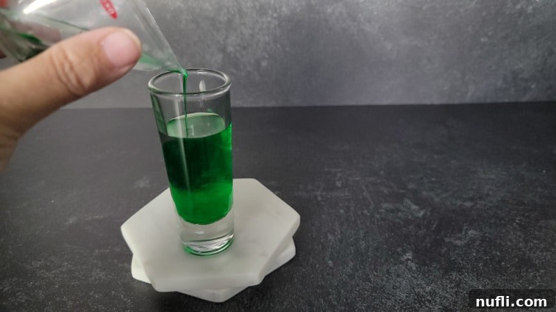 Green liquid pouring into shot glass on two marble coasters