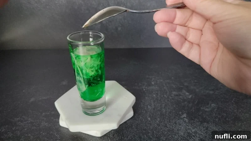 Spoon held upside down above a shot glass with green and cream liquid
