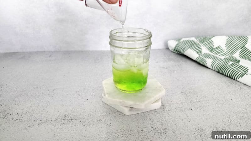 Easy Scooby Snack Shot Recipe 4 Clear liquid pouring into a small mason jar with green liqueur in it for a Scooby Snack Shot