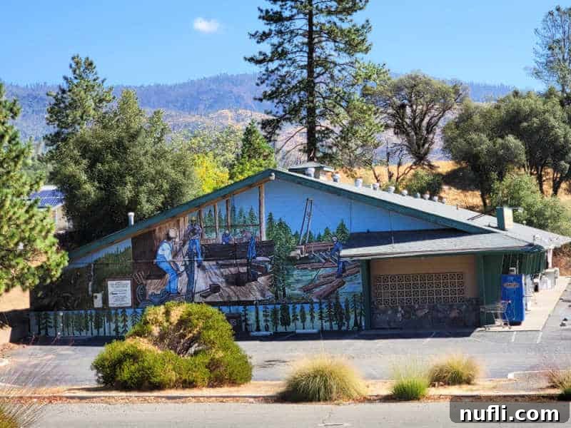 Logging mural on the side of a building with trees and mountains in the background