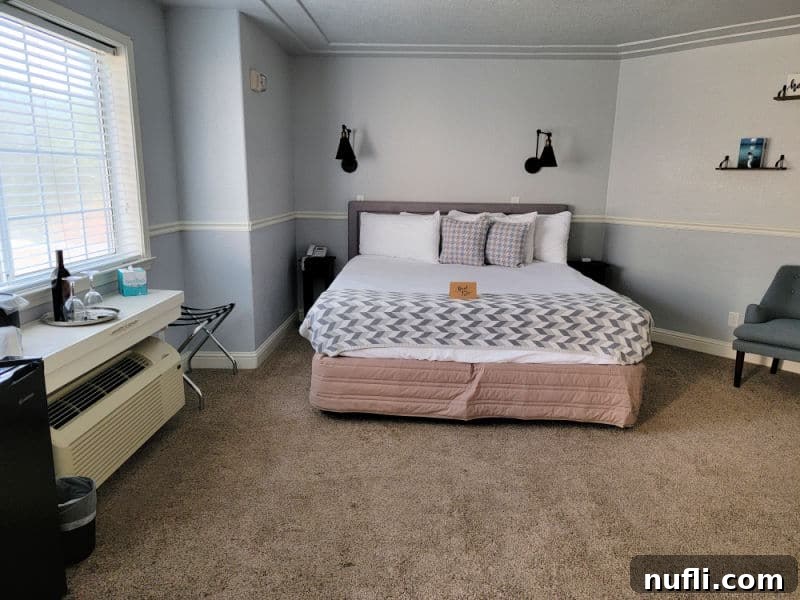 bed in the middle of a room with a counter holding wine and glasses near a chair