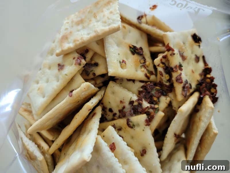 The spicy ranch seasoning mixture being poured over saltine crackers inside a sealed plastic bag.