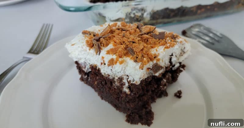 square of Butterfinger poke cake on a white plate next to forks