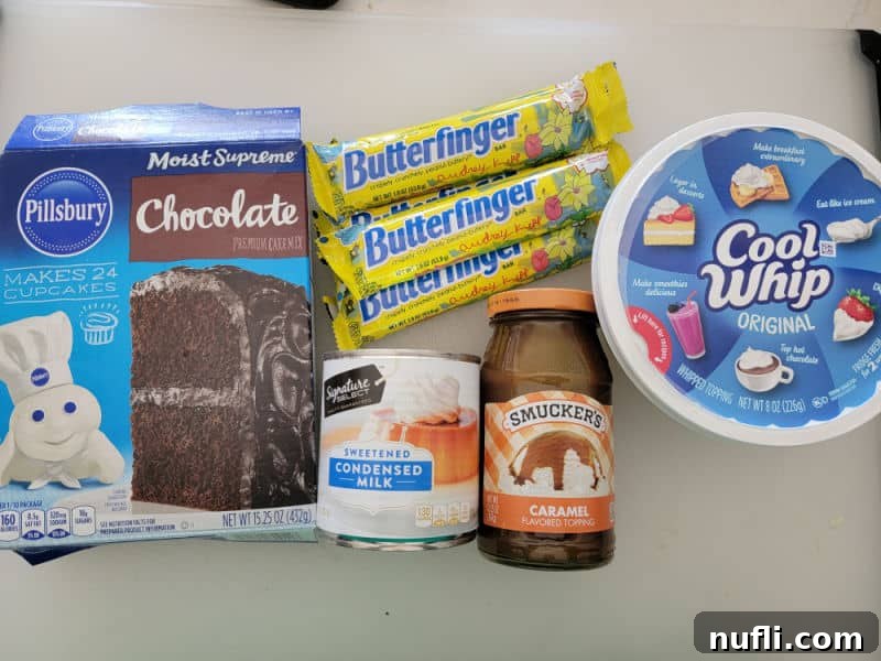 Butterfinger poke cake ingredients, chocolate cake mix, Butterfinger candy bars, cool whip, sweetened condensed milk, and caramel topping on a white counter