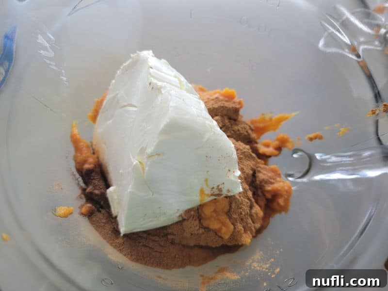 A glass batter bowl containing softened cream cheese and canned pumpkin puree, ready to be mixed into a creamy base for the pumpkin dip.