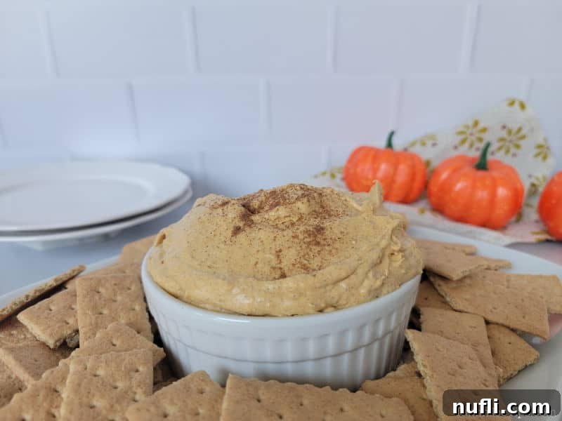 A festive white bowl filled with Pumpkin Cream Cheese Dip, beautifully garnished and encircled by an inviting arrangement of graham crackers, highlighting its readiness for a fall gathering.