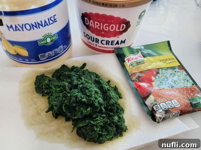 Knorr Spinach Dip Effortless Entertaining 3 A vibrant flat lay shot displaying the core ingredients for Knorr Spinach Dip: creamy mayonnaise, rich sour cream, fresh green spinach, and the essential Knorr vegetable dip mix, ready for preparation.