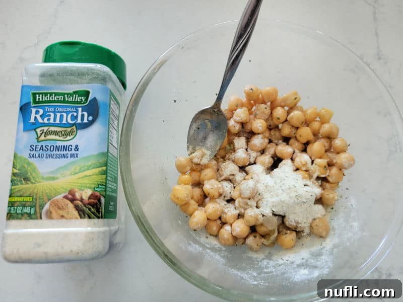 Hidden Valley Ranch dressing mix next to a glass bowl with seasoned chickpeas and a spoon