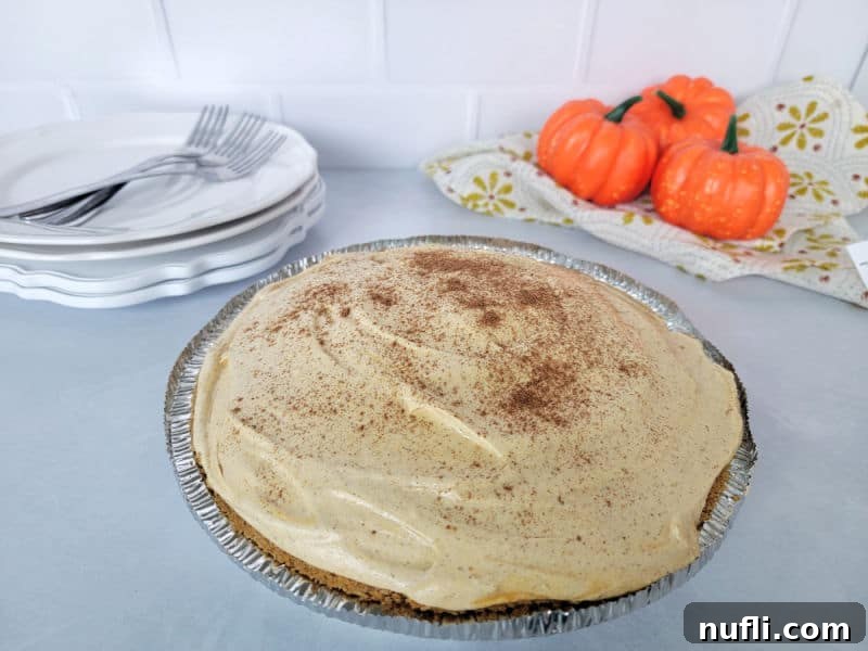 No bake pumpkin pie in a pie dish next to mini pumpkins and a stack of plates and forks. 