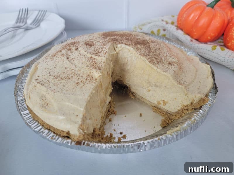 No bake pumpkin pie in a pie dish with a slice missing next to a stack of plates and forks